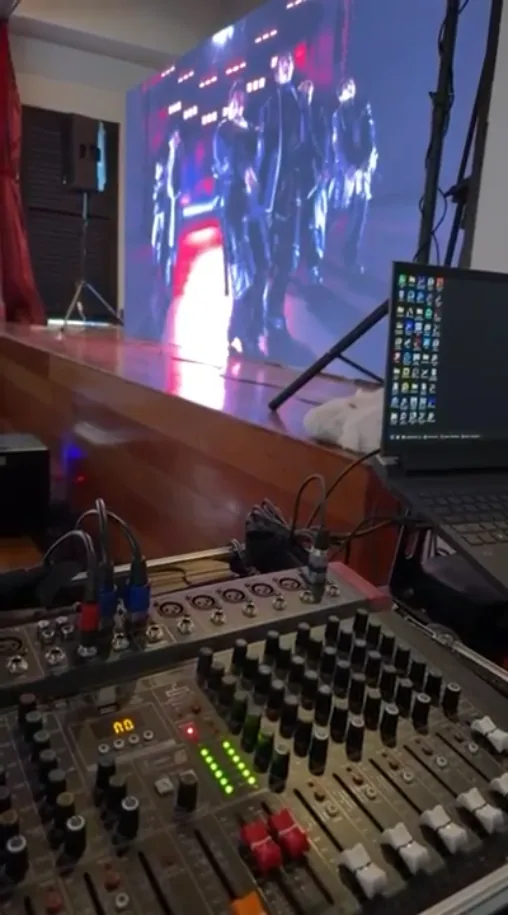 Mesa de som e notebook diante do painel de LED exibindo um show ao vivo