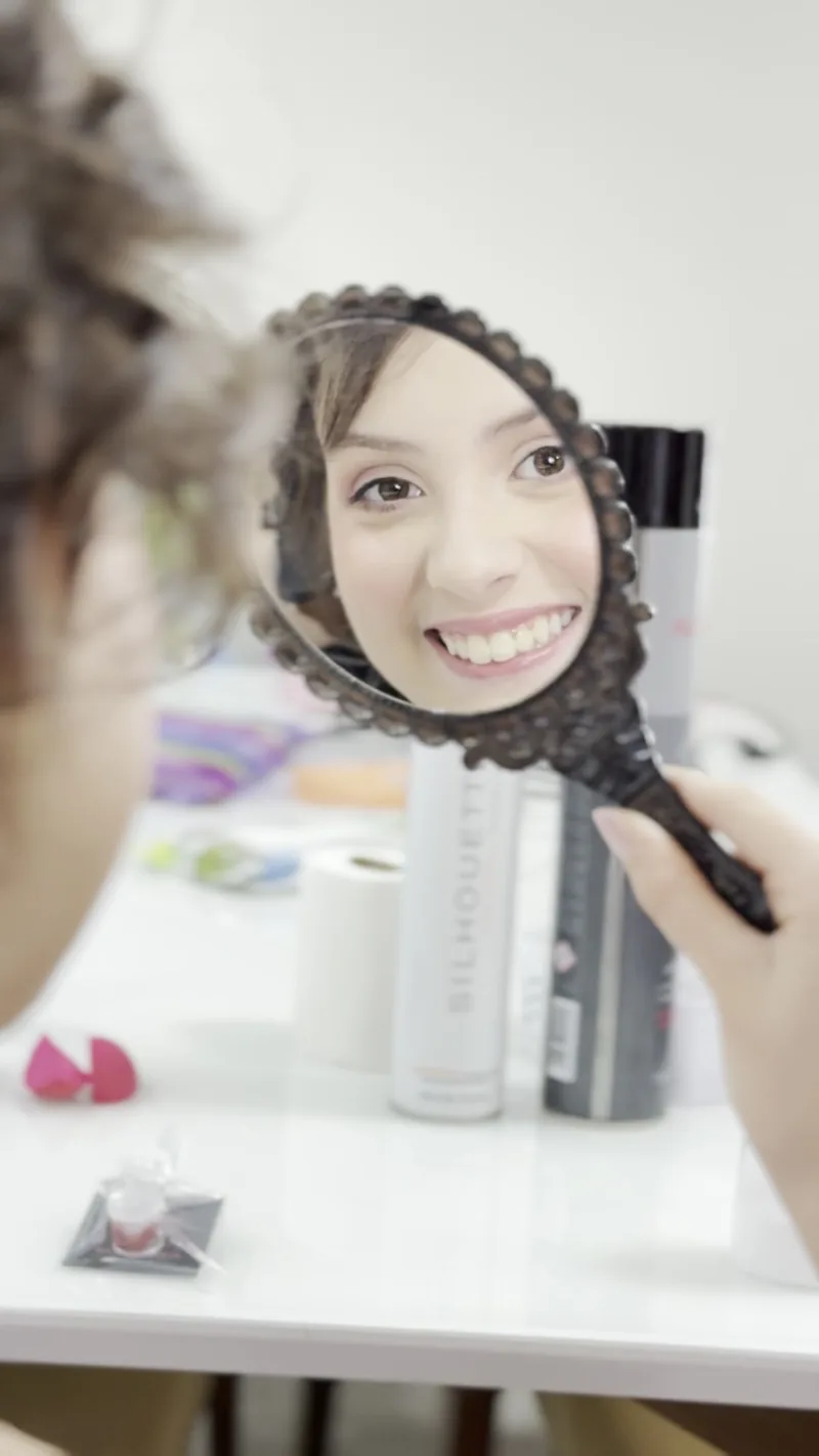 Cliente se vendo pronta no espelho de mão, sorrindo