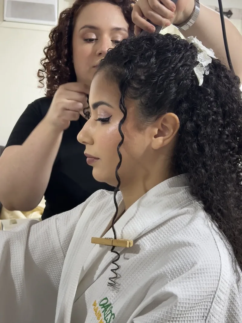 Detalhe das mãos prendendo o arranjo de flores no cabelo cacheado